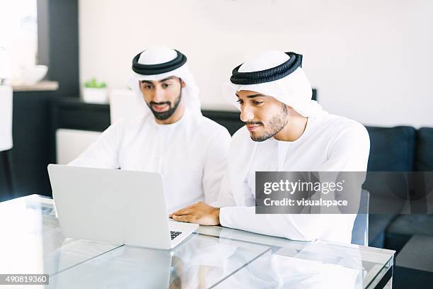 two arab friends watching videos on laptop - emirati laptop stock pictures, royalty-free photos & images