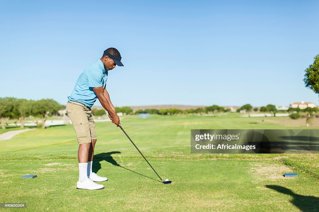 African golfer looking at the ball, ready to hit it.