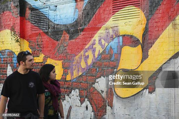 People walk past murals showing the German flag on the day before the 25th anniversary of German reunification on October 2, 2015 in Berlin, Germany....