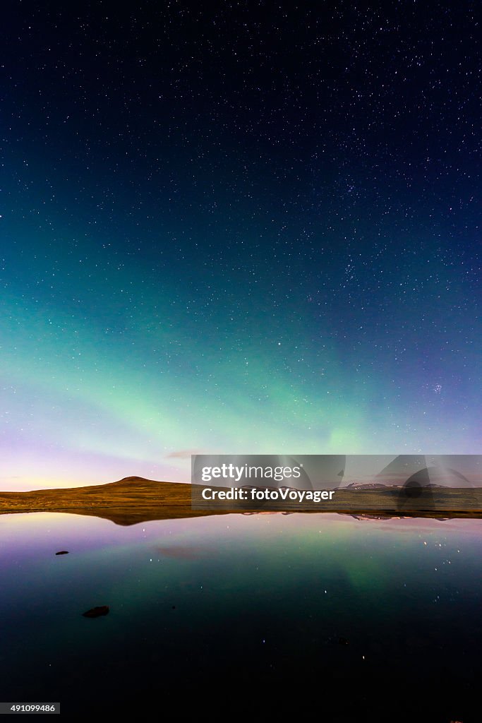 Aurora and glittering stars reflecting in tranquil mountain lake Iceland