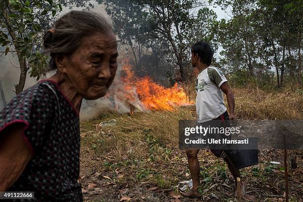 Man carries a bucket of water as they try to extinguish the fire on burned peatland and fields near his house at Ogan Ilir district on October 3,...