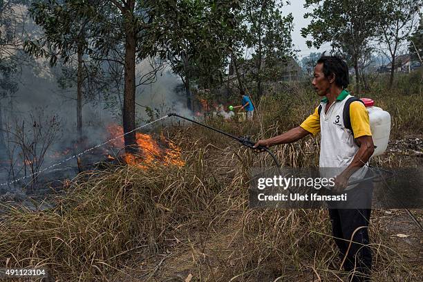 Man sprays the water as they extinguish the fire on burned peatland and fields near his house at Ogan Ilir district on October 3, 2015 in Palembang,...