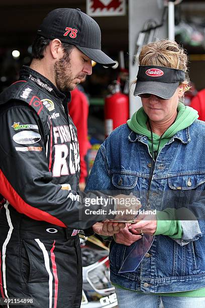 Martin Truex Jr., driver of the Furniture Row/Visser Precision Chevrolet, left, signs his autograph for a fan in the garage area during practice for...