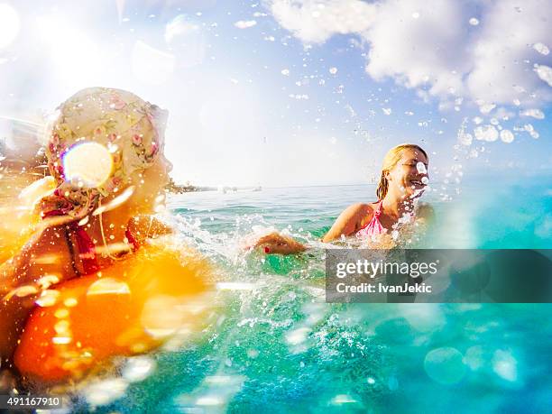 mother and daughter splashing water in sea - mother and child in water at beach stock pictures, royalty-free photos & images