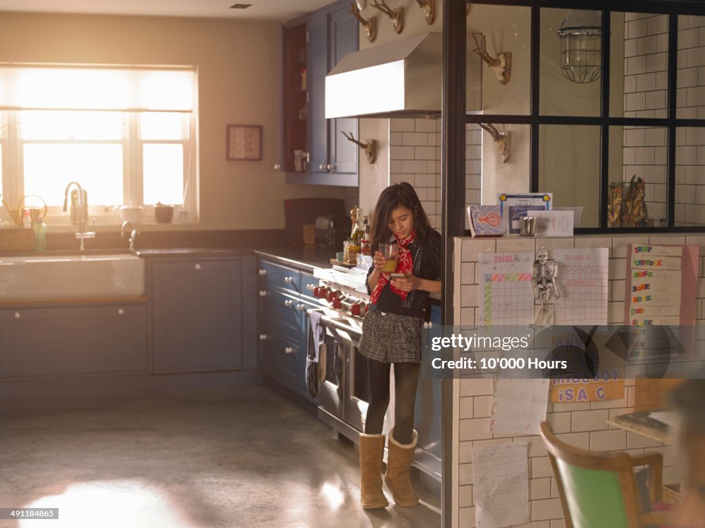 Girl standing in a sunny kitchen looking at phone