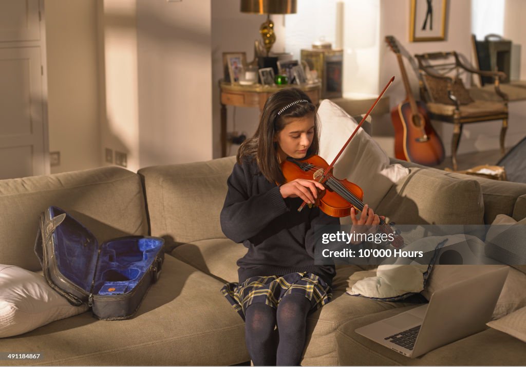 Schoolgirl practising the violin, using a laptop
