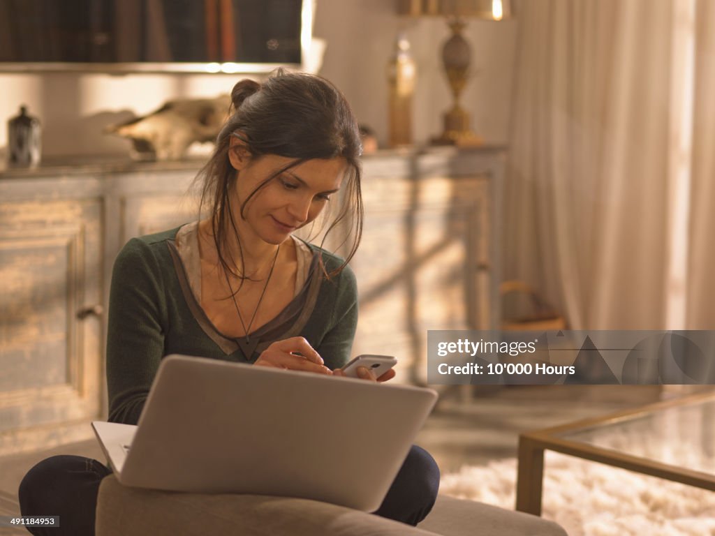 A woman at a laptop looking at her phone