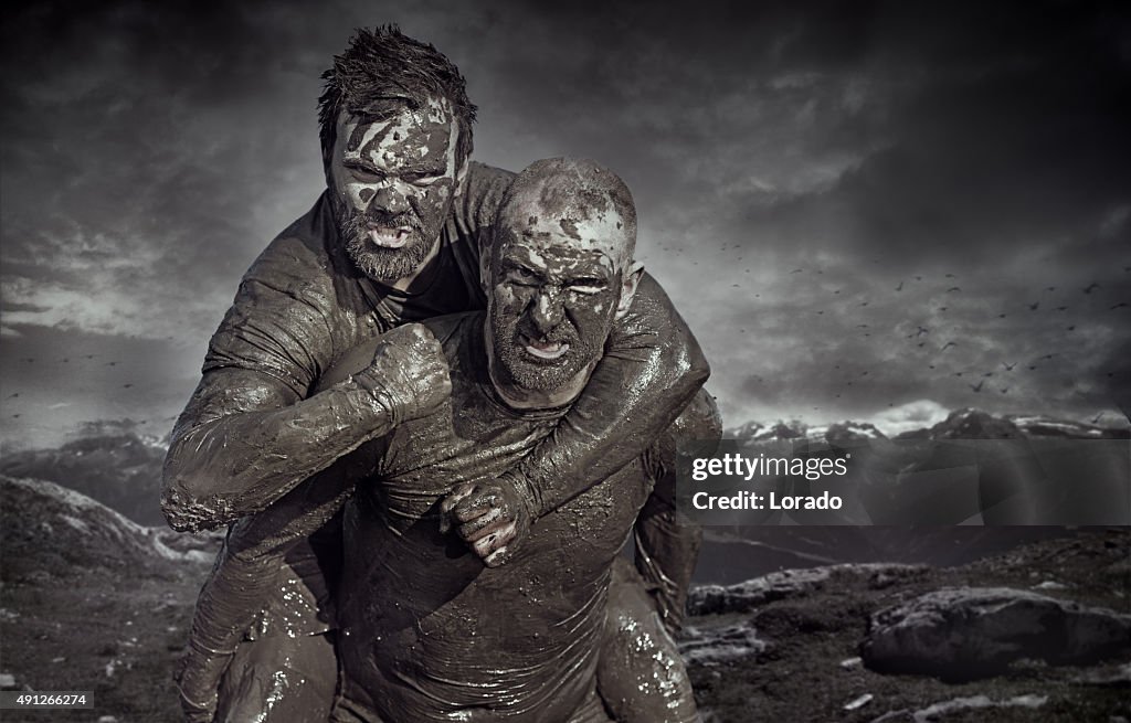 Shaved man carrying friend during a mud run