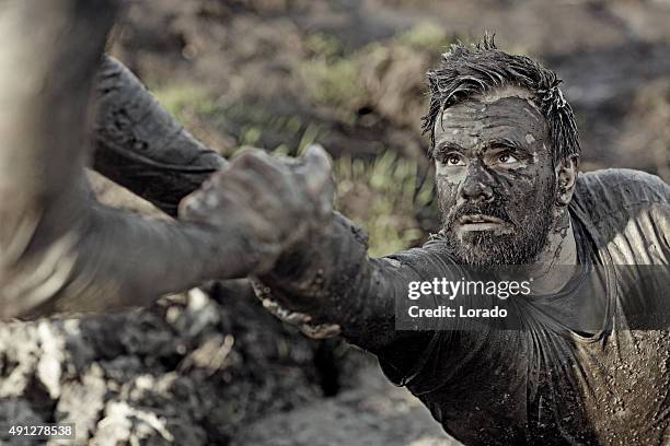 mann hilft seiner freundin mit anreise von schlamm - hindernisparcours stock-fotos und bilder