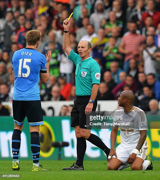 Referee Mike Dean shows Eric Dier of Tottenham Hotspur a yellow card during the Barclays Premier League match between Swansea City and Tottenham...