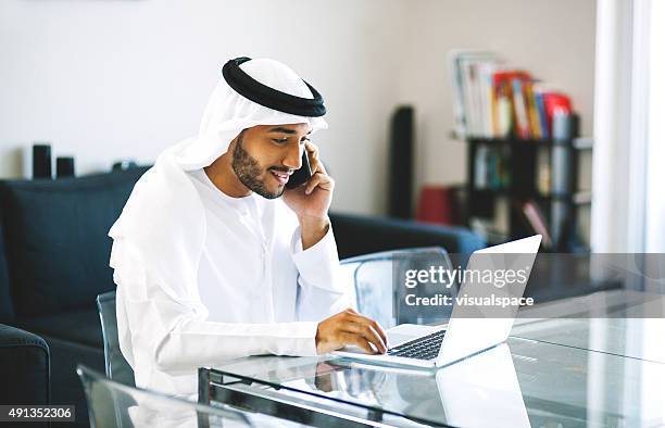 junge arabische mann am telefon beim surfen - emirati guy using laptop stock-fotos und bilder