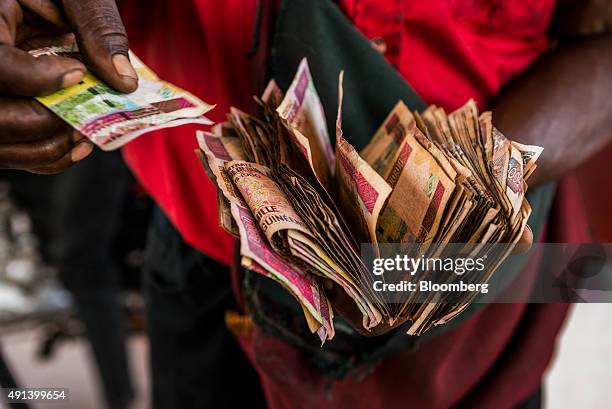An employee counts Guinean franc banknotes on the forecourt of a gas station operated by Total SA in Kamsar, Guinea, on Monday, Sept. 7, 2015. With...