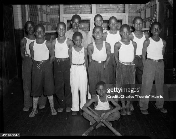 Group portrait of twelve young men and boys, most wearing light colored undershirts, including boy seated on floor holding two baseball bats, in...