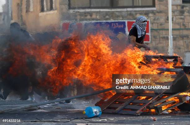 Palestinian stone throwers stand next to a burning wood barrier during clashes with Israeli security forces in the Palestinian neighborhood of...