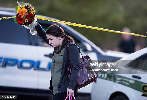 Woman navigates crime scene tape as she holds flowers on the campus of Umpqua Community College as it reopens on October 5, 2015 in Roseburg, Oregon....