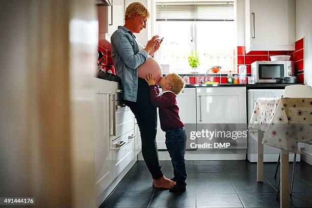 pregnant woman with her son in the kitchen - belly kissing stock pictures, royalty-free photos & images