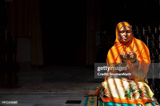 mid-adult muslim woman praying, with folded hands - muslim woman darkness stock pictures, royalty-free photos & images