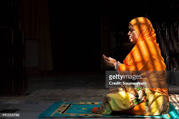 mid-adult muslim woman praying, with folded hands - muslim woman darkness stock pictures, royalty-free photos & images