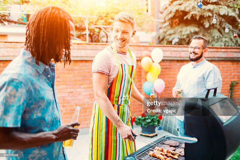 Young Men Grilling Meat At Barbecue Party.