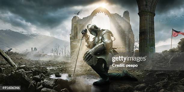 medieval knight kneeling with sword in front of building ruin - fortress stockfoto's en -beelden