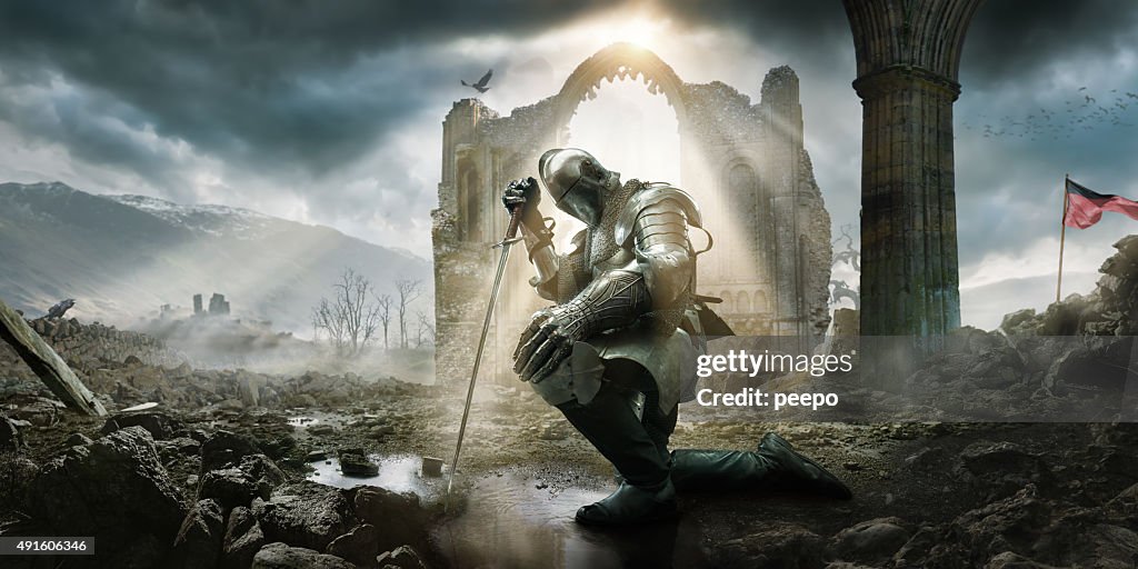 Medieval Knight Kneeling With Sword In Front of Building Ruin