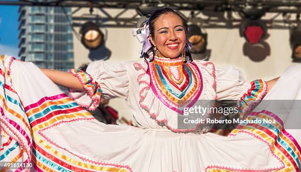 Young women in white costume with colorful stripes performing Mexican folk dance on stage at MexFest 2015, Toronto. MexFest 2015 is celebration of...