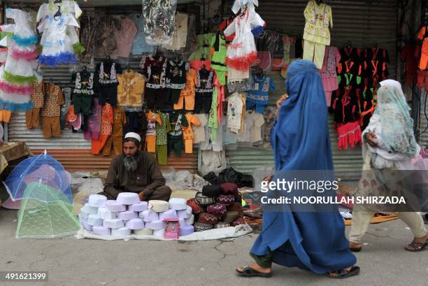 An Afghan street vendor waits for customers as a burqa-clad woman walks past on a street in Jalalabad on May 16, 2014. Some nine million Afghans or...