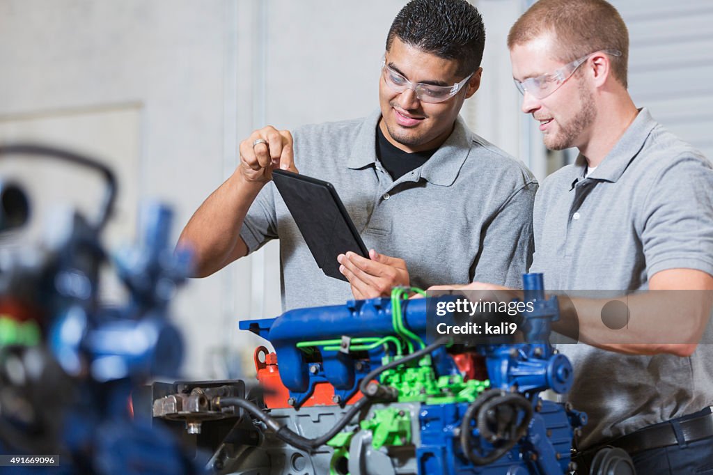 Two multi-racial men in auto mechanic school with engine