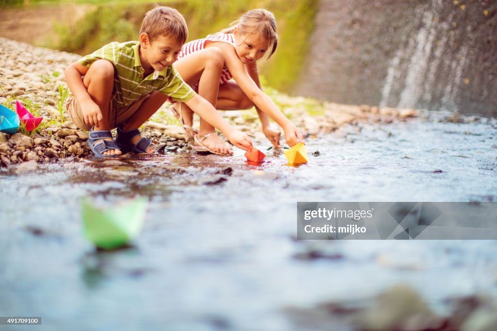 Boy and girl playing paper boats on the river