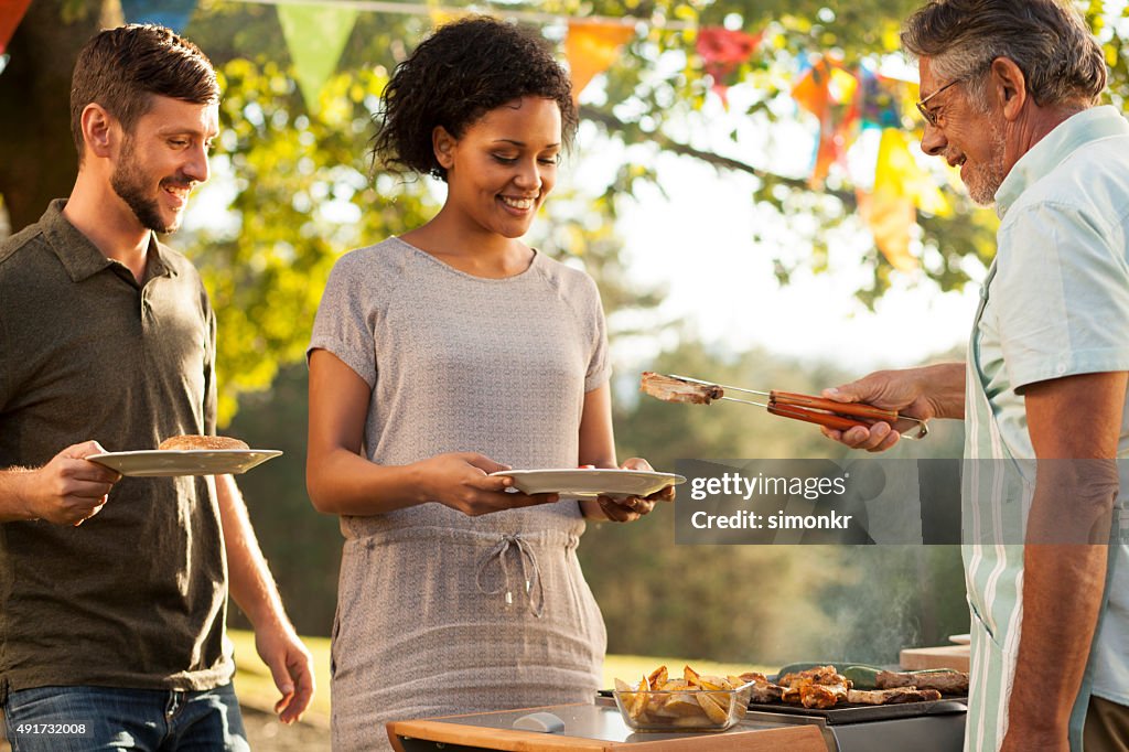 Senior man serving grilled meat to his son and daughter-in-law