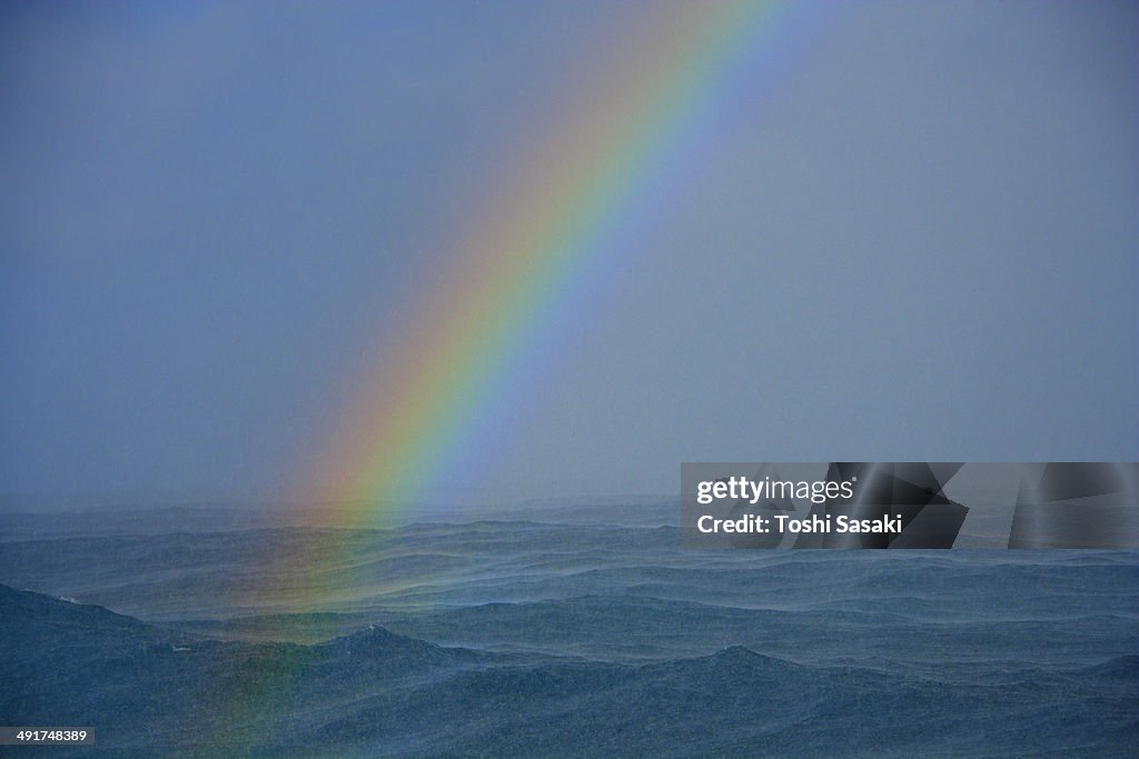 Rainbow appears at rainy ocean at dusk