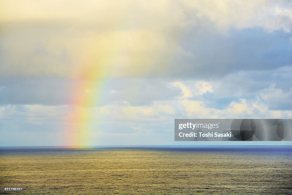Rainbow appears at glowing ocean at sunset