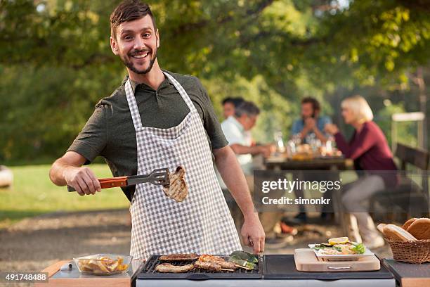 portrait of man grilling meat at barbecue outdoors - barbecue man stock pictures, royalty-free photos & images