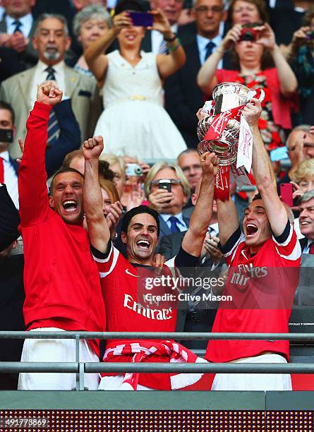 Captain Thomas Vermaelen of Arsenal lifts the trophy in celebration alongside Lukas Podolski and Mikel Arteta after the FA Cup with Budweiser Final...