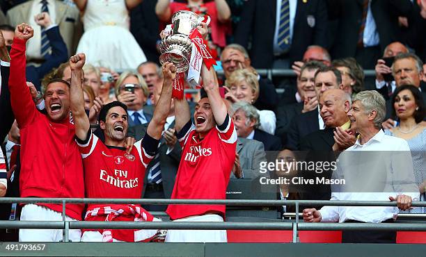 Captain Thomas Vermaelen of Arsenal lifts the trophy in celebration alongside Lukas Podolski , Mikel Arteta and Arsene Wenger manager of Arsenal...