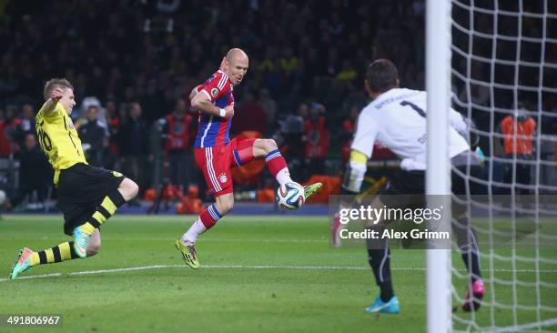 Arjen Robben of Bayern Muenchen scores his team's first goal against goalkeeper Roman Weidenfeller and Lukasz Piszczek of Borussia Dortmund during...