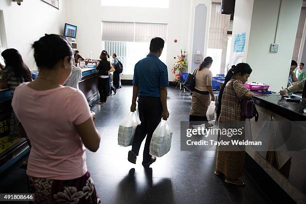 Bank employee carries two bags of kyat to a customer's waiting car at the KBZ Bank main office on October 8, 2015 in Yangon, Burma. In Burma, the...