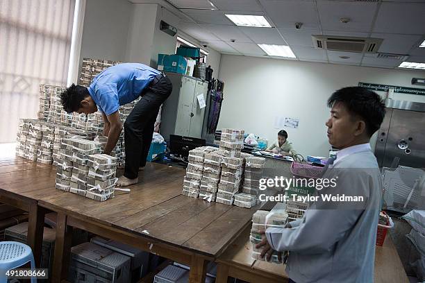 An employee climbs on a table to stack 1,000 kyat notes at the KBZ Bank main office on October 8, 2015 in Yangon, Burma. In Burma, the most widely...