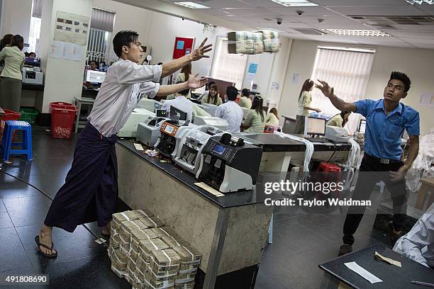Employees throw stacks of money to be piled on the floor for a customer's withdrawal at the KBZ Bank main office on October 8, 2015 in Yangon, Burma....