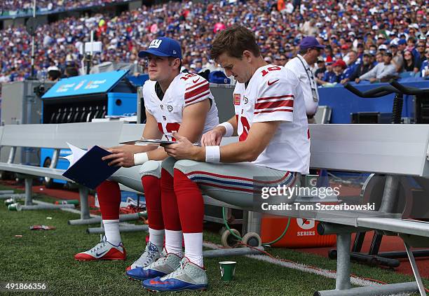Eli Manning of the New York Giants reviews a playbook on the bench beside backup Ryan Nassib during NFL game action against the Buffalo Bills at...