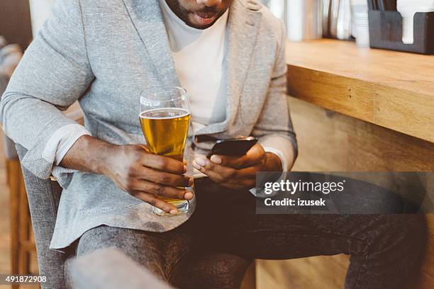 afro american man sitting in the pub, using smart phone - african american restaurant texting stockfoto's en -beelden