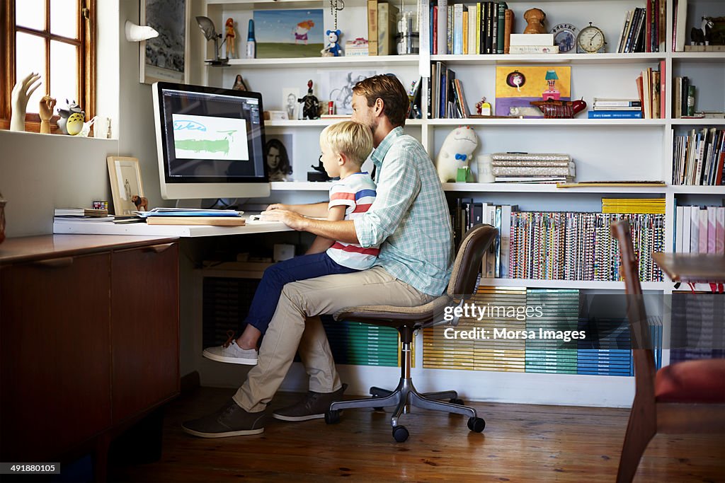 Boy sitting on father's lap at computer desk