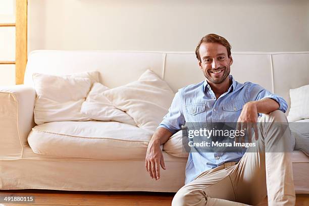 portrait of smiling man leaning against sofa - sitting on floor fotografías e imágenes de stock