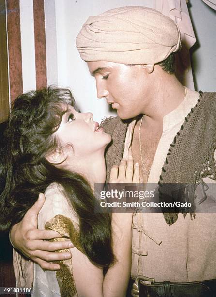 Elvis Presley, wearing a turban and Middle Eastern costume, holding Mary Ann Mobely, who clutches his chest and looks distraught, in a film still...