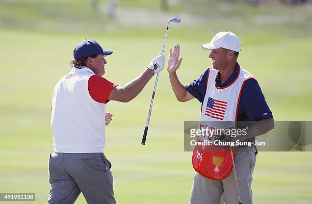 Phil Mickelson of the United States Team celebrates with his caddie Jim Mackay after holing a bunker shot on the 12th hole during the Friday...
