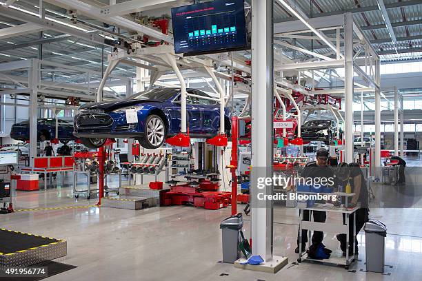 Employees stand by a work bench as Tesla Model S automobiles stand on raised cradles on the battery pack and driving unit assembly line at the Tesla...