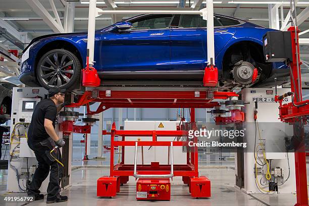 An employee fits a battery pack under a Tesla Model S automobile on the final assembly at the Tesla Motors Inc. Factory in Tilburg, Netherlands, on...