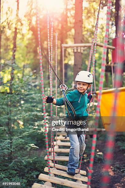 kleiner junge zu fuß auf ropes course in outdoor adventure park - hochseilgarten stock-fotos und bilder