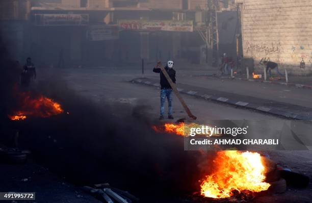 Masked Palestinian protester burns tires during clashes with Israeli security forces in the Palestinian neighborhood of Shuafat refugee camp in east...
