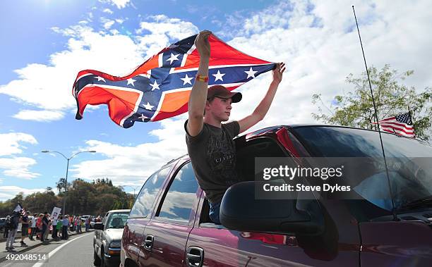 Chance White holds a confederate flag as he drives past protesters lining the street in front of the Roseburg Regional Airport on October 9, 2015 in...